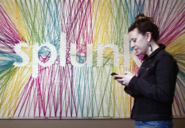 A photo of a woman looking down at her mobile device as she walks by a Splunk logo sign.