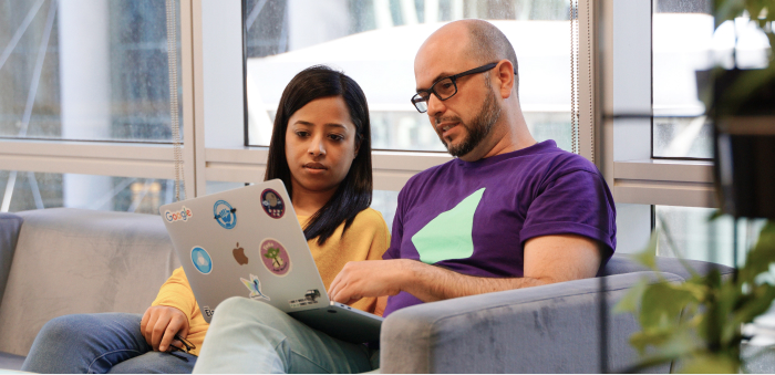 Dos empleados de Iress sentados en un sofá mirando una computadora portátil