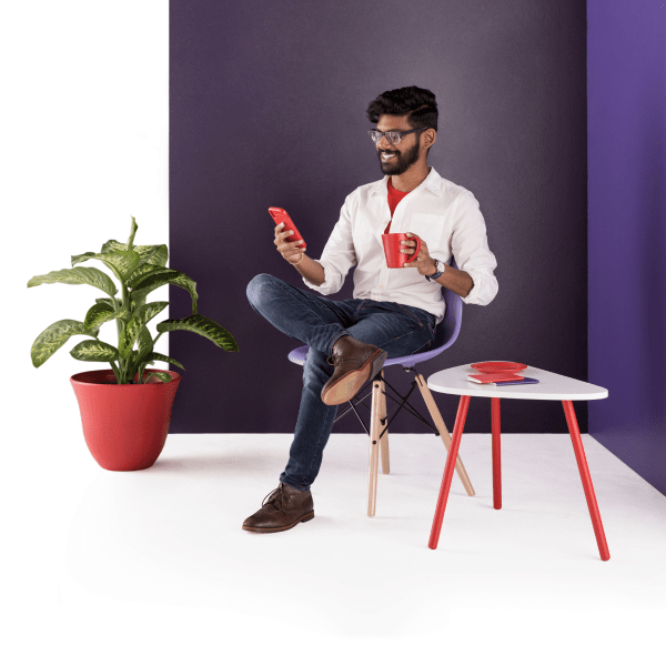 A man sits in a chair. He smiles warmly at the mobile phone in hand as coworkers post their status updates in Slack.