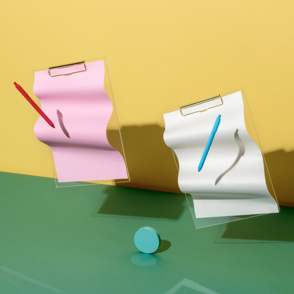 Stylised clipboards and pens suspended over a colourful desk and backdrop.