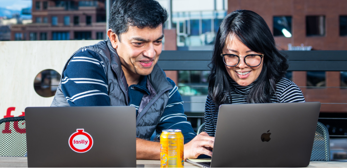 Zwei Mitarbeiter von Fastly arbeiten über ihren Laptops auf einer Büroterrasse im Freien zusammen.