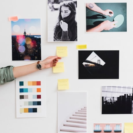 Arm placing a sticky note on a wall alongside sticky notes and photographs