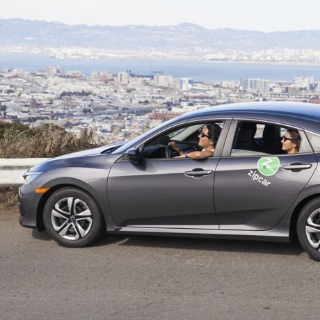 Friends in a Zipcar vehicle driving along a scenic road