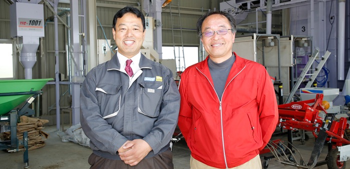 カクイチの社員 2 名が農機具を収納する倉庫内に立っている写真