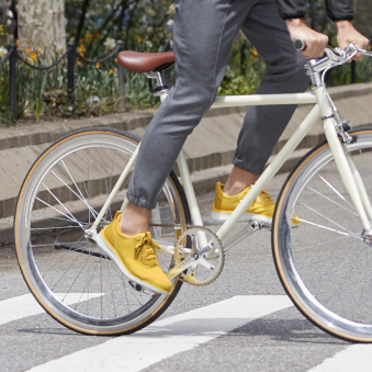 'A cyclist wears yellow Cole Haan sneakers while pedaling through a crosswalk.'