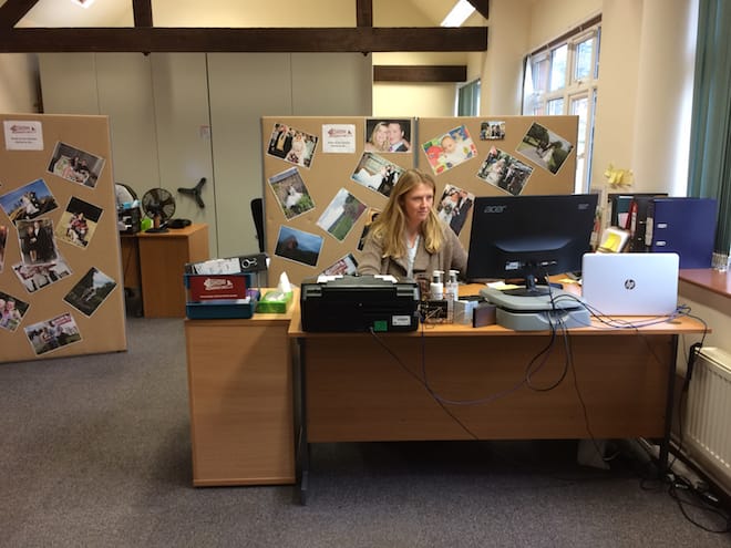 Lucy sits at a computer responding to email. Wedding pictures are posted around her cubicle.