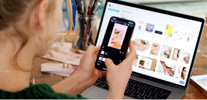 Eine Person, die Benachrichtigungen auf einem Smartphone anschaut, und ein Laptop im Hintergrund.