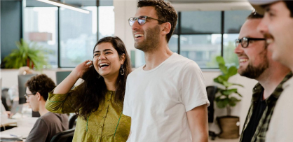Eine Gruppe von Mitarbeitern und Mitarbeiterinnen, die im Büro miteinander lachen und zusammenarbeiten.